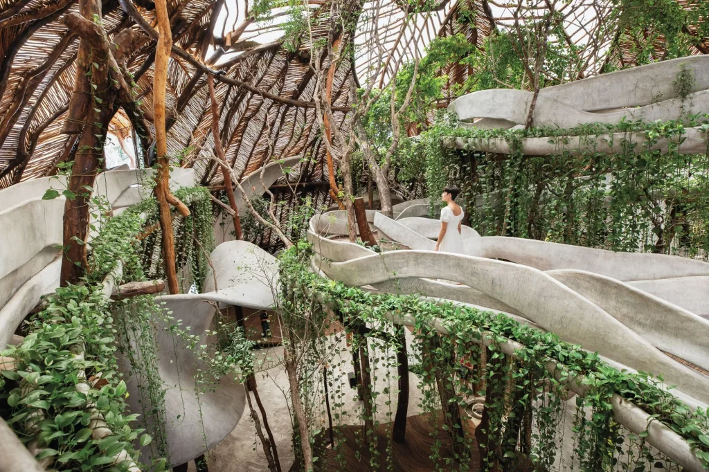 In an increasingly urban world, the desire to reconnect with nature has never been stronger. Concrete cities, glowing screens and fast-paced living have left many yearning for balance and calm — a space to breathe. Enter biophilic design, a philosophy that places nature at the heart of how we build and live. The term, rooted in the Greek word biophilia meaning “love of life,” captures the human instinct to seek connection with the natural world. Unlike fleeting design trends, biophilic design is a movement that redefines how we think about space. It is not about adding a few plants to a corner but creating environments that emulate the patterns, materials and rhythms of nature itself. Whether through daylight, greenery, natural textures or organic shapes, biophilic design invites the outdoors in, transforming interiors into sanctuaries that nurture both body and mind. The Philosophy Behind Biophilic Design The concept gained prominence in the 1980s through American biologist Edward O. Wilson, who proposed that humans are innately drawn to nature. Modern life, however, often isolates us from it. Biophilic design bridges that gap by weaving natural elements into built environments, restoring a sense of balance. The philosophy is grounded in three key principles — nature in the space, nature of the space and natural analogues. The first includes direct contact with elements like plants, light, air and water. The second captures spatial qualities that mimic natural environments, such as refuge, prospect and mystery. The third focuses on materials and patterns that reflect natural forms, like stone textures, wooden grains and biomorphic shapes. Together, these principles work to enhance our sensory experience and emotional wellbeing, reminding us that we are not separate from nature but a part of it. Why It Matters Science has long supported what intuition already knows — proximity to nature improves our health and happiness. Studies show that interiors designed with natural light, greenery and organic materials can reduce stress, enhance concentration and even boost productivity. In homes, this translates into calmer, more restorative spaces. In workplaces, it fosters creativity and engagement. The benefits extend beyond mood and performance. Biophilic design can also improve air quality, regulate temperature and reduce noise, creating environments that are not only beautiful but also healthier to live in. As climate change and urbanisation reshape the planet, design that respects and reconnects us with nature feels not just desirable but essential. The Look and Feel of Biophilic Interiors Biophilic spaces are defined by a subtle yet immersive sense of natural harmony. Sunlight becomes a design feature, filtering through large windows or skylights. Indoor plants — from sculptural fiddle leaf figs to hanging ferns and moss walls — bring life to interiors, softening hard lines and purifying the air. Materials play a crucial role. Wood, stone, clay, rattan and bamboo evoke an organic authenticity that manufactured surfaces rarely achieve. Natural fabrics like linen, cotton and wool add warmth and texture. Colours are drawn from the earth and sky — greens, browns, creams, and soft blues that mirror the landscapes we find most calming. Water features, such as small fountains or reflecting pools, add movement and sound that soothe the senses. Even artwork inspired by nature or furniture shaped with flowing, organic lines contributes to the overall atmosphere of connection and calm. Designing with Biophilia in Mind Creating a biophilic home does not require a total redesign. It begins with intention — finding ways to bring nature closer to everyday living. Start by maximising natural light: sheer curtains, mirrors and open layouts can make a remarkable difference. Introduce plants of varying sizes and textures, grouping them to mimic natural clusters rather than scattering them randomly. Choose furniture made from sustainable materials and keep the colour palette soft and earthy. Incorporate tactile surfaces such as woven baskets, textured rugs and raw wood finishes. Ensure good airflow and avoid synthetic fragrances — fresh air and natural scents are the essence of biophilic living. Finally, think beyond the visual. Biophilic design engages all the senses: the sound of trickling water, the scent of fresh herbs, the feel of linen sheets, and the sight of sunlight shifting across the floor. Each element works together to create a space that feels alive, restorative and deeply human. The Future is Green Biophilic design is more than an aesthetic choice; it is a response to how we want to live in the future — sustainably, mindfully and in harmony with the natural world. As architects and designers increasingly embrace this philosophy, our cities and homes are evolving into greener, gentler places that support both people and planet. By bringing nature indoors, biophilic design does not just beautify our spaces. It heals them. It reminds us that true comfort lies not in excess but in coexistence, and that the most inspiring interiors are those that reflect the living world around us