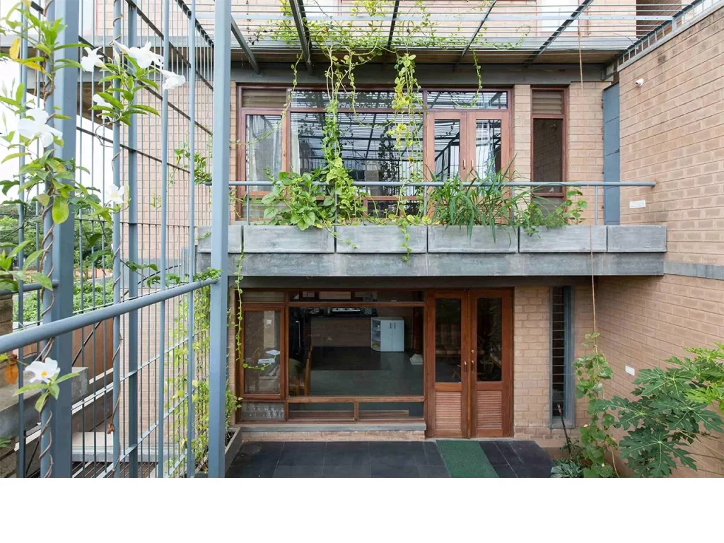 In an era obsessed with glass towers, imported stone, and air-conditioned excess, Chitra Vishwanath did something borderline rebellious: she picked up mud — and built the future. While the architectural world sprinted toward shiny facades and carbon-heavy vanity, she stayed rooted, almost literally, in the soil beneath her feet. Her buildings don’t scream; they exhale. They don’t dominate landscapes; they collaborate with them. And in a city like Bengaluru, where the climate is changing faster than the skyline, Vishwanath’s work is a quiet but powerful reminder that sustainability isn’t a trend. It’s good design with its conscience intact. A Childhood Shaped By Ecology And Curiosity Chitra Vishwanath’s early fascination with nature, resourcefulness, and the quiet intelligence of traditional craft laid the groundwork for her design philosophy. Growing up in an India where nothing was wasted and everything was repurposed, she developed an instinctive understanding that architecture wasn’t about spectacle — it was about function, climate, community, and care. That sensibility would later become the spine of her work. Choosing Earth When The World Chased Concrete By the 1990s, when Indian cities were racing to embrace glass-heavy, imported-material “modernity,” Vishwanath calmly charted a different path. Instead of concrete and metal, she chose mud — specifically, stabilised earth blocks. Her reasoning was both scientific and ethical. Earth has low embodied energy, regulates temperature naturally, and is readily available. It’s recyclable, breathable, and culturally rooted. By building her own Bengaluru home out of earth, she demonstrated that sustainability wasn’t theoretical. It was practical, local, resilient, and affordable. The Science Behind Earthy Aesthetic What looks simple in her buildings is often anything but. Behind the raw textures and warm tones lie sophisticated systems that make the architecture perform beautifully without relying on energy-hungry technologies. Natural ventilation replaces air conditioners. Rainwater harvesting is integrated from the blueprint stage. Greywater loops keep waste out of the sewage system. Traditional building know-how meets contemporary structural engineering. Vishwanath doesn’t beautify sustainability — she operationalises it until it becomes the default, not the exception. Biome Environmental Solutions As A Laboratory Of Ecology At Biome Environmental Solutions, the firm she leads, sustainability isn’t a buzzword — it is the organising principle. Architects work alongside ecologists, hydrologists, and community experts to design buildings, water systems, landscapes, and public infrastructure that function as interconnected ecological units. The firm’s work extends far beyond architecture: groundwater recharge, wetlands revival, wastewater management, and ecological urbanism have become core to its mission. In many ways, Vishwanath is designing ecosystems as much as structures. A Philosophy Rooted In People And Planet Chitra Vishwanath’s architecture consistently places human comfort, material honesty, and environmental responsibility above visual theatrics. Her buildings are modest in scale, deeply functional, cost-conscious, and free of ego. She believes that beauty emerges naturally when a structure responds intelligently to climate, culture, and context. Her aesthetic — warm, tactile, grounded — is a byproduct of those values rather than a stylistic ambition. Challenging The Illusion That Modern Means Glass In rapidly urbanising cities, the idea of “modern” architecture is often equated with sealed buildings, reflective facades, and mechanical cooling systems. Vishwanath dismantles that notion with precision. To her, modernity is measured by intelligence, not appearance. A building is modern if it consumes less energy, interacts with natural forces, manages its water responsibly, uses local materials, and leaves a small ecological footprint. Her definition resets the conversation — and it’s one the climate desperately needs. Projects That Shifted The Sustainability Conversation Several of Vishwanath’s projects have become touchstones in India’s sustainable architecture movement. Her own residence and office demonstrate how an urban building can be almost entirely self-sufficient. Schools and community structures she has designed show the scalability of earth architecture. Her water-sensitive urban planning projects have influenced how neighbourhoods and cities view groundwater, stormwater, and sewage. Each project becomes a case study, not only in design but in ecological logic. Craftspeople As Partners In Innovation A crucial, often overlooked dimension of her work is the role of skilled masons and craftspeople. Vishwanath treats them not as labourers but as co-creators. Their knowledge of traditional construction techniques and material behaviour becomes as essential as the architect’s drawings. On her sites, learning flows in every direction — craftspeople adopt new scientific methods, and architects gain insight from centuries-old skills. This collaborative ecosystem strengthens livelihoods while keeping traditional craftsmanship alive. A Legacy That Offers India A Blueprint For Resilience In a country facing climate unpredictability, water scarcity, and urban stress, Chitra Vishwanath’s work stands as a blueprint for the future. Her designs prove that sustainability isn’t a compromise — it’s an upgrade. She has shown that buildings can be cost-effective, climate-responsive, culturally rooted, and aesthetically compelling without exhausting the planet. Her legacy is not just architectural. It is ecological, social, and systemic. By choosing earth, she gave Indian architecture something far more enduring than a style — she gave it a conscience