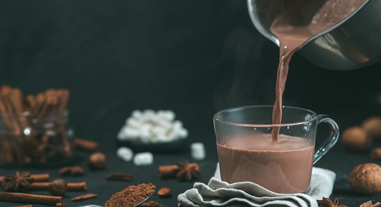 Pouring tasty cocoa drink into mug on table